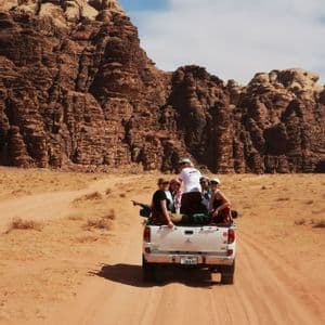 Un voyage de groupe WeRoad à l'arrière d'un pick-up blanc sur une route sablonneuse à travers un désert rocheux.
