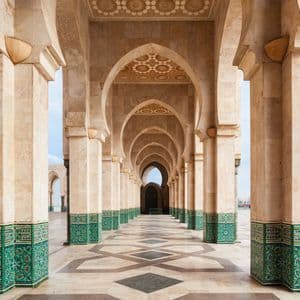 Une vue le long d'une longue colonnade de piliers en pierre et d'arches mauresques, avec des détails en carreaux verts et un sol à motifs.