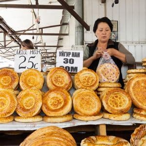 Una donna in una bancarella del mercato che vende pagnotte di pane rotonde e decorate ne mette una in un sacchetto di plastica.