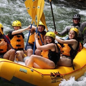 Un grupo de WeRoad sonríe mientras hace rafting en un río de aguas rápidas, llevando cascos y chalecos salvavidas.