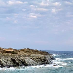 Ein schwarz-weiß spiralförmiger Leuchtturm steht auf einer felsigen Klippe mit Blick auf das Meer unter einem bewölkten Himmel.