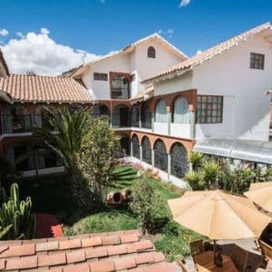 Una vista dall'alto del cortile di un hotel con mura bianche, tetti di tegole rosse, archi in mattoni e un giardino centrale.