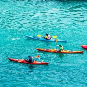 Desde arriba, cuatro personas en un viaje grupal de WeRoad reman kayaks de colores en aguas turquesas.