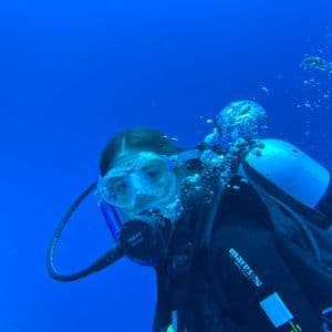 Una toma de primer plano de un buzo con máscara y regulador, flotando bajo el agua en aguas azul profundo con burbujas ascendiendo.