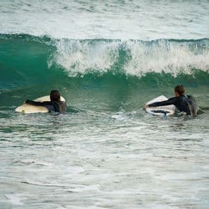 Due persone in muta galleggiano sulle loro tavole da surf nell'oceano mentre un'onda si infrange dietro di loro.