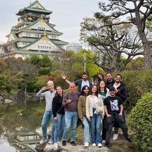 Un viaggio di gruppo WeRoad in posa su delle rocce vicino a uno stagno, con un tradizionale castello giapponese e alberi sullo sfondo.