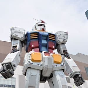 Una inquadratura dal basso di una statua gigante a grandezza naturale del robot Gundam, posta di fronte ad alti edifici moderni.