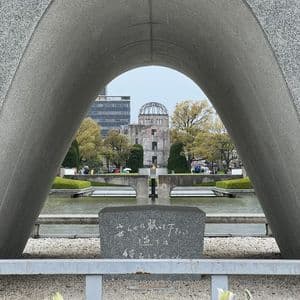 Vista attraverso un grande arco commemorativo in granito che incornicia una rovina a cupola e una fiamma su una vasca d'acqua in un parco.