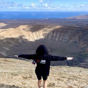 Un accompagnatore WeRoad sta con le braccia aperte sul bordo di un grande cratere vulcanico, affacciato sul mare.