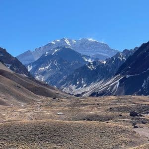 Un vasto valle seco con vegetación escasa conduce hacia una sierra maciza y nevada bajo un cielo azul claro.