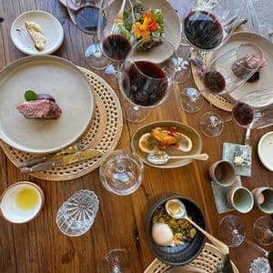 Una mesa de madera vista desde arriba, con varios platos gourmet y copas de vino tinto para un maridaje.