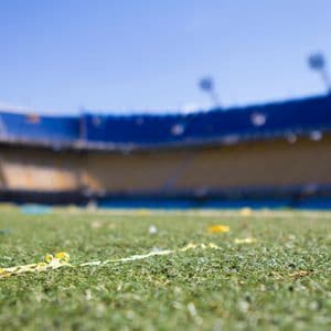 Primer plano en contrapicado de confeti amarillo sobre el césped de un estadio, con gradas azules y amarillas borrosas al fondo.