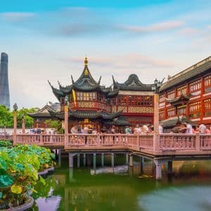 Una pagoda tradizionale cinese su uno stagno con foglie di loto, con un moderno grattacielo sullo sfondo e persone su un ponte.