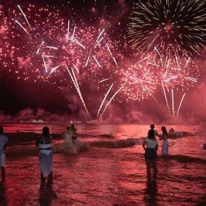 Un gruppo WeRoad in viaggio di notte in mare osserva fuochi d'artificio rossi che esplodono nel cielo.