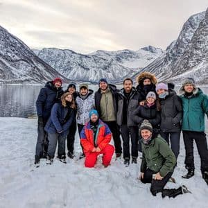 Eine WeRoad-Gruppe lächelt für ein Foto in verschneiter Landschaft mit Fjord und Bergen im Hintergrund.