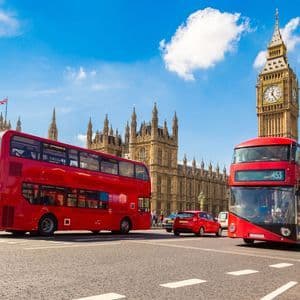 Deux bus rouges à impériale sur une rue avec les Chambres du Parlement et Big Ben en arrière-plan sous un ciel bleu.