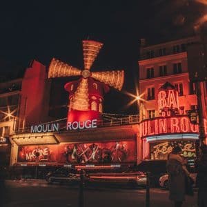 L'edificio del Moulin Rouge di notte, con il suo iconico mulino a vento rosso e le insegne al neon illuminate brillantemente sopra una strada trafficata.