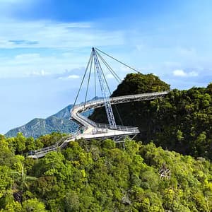 Eine gewundene Fußgänger-Himmelsbrücke, die von einem einzelnen Pylon über einem dichten grünen Wald auf einem Berg hängt.