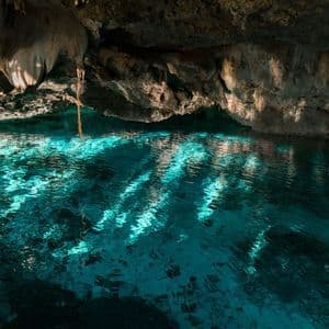 La luce del sole illumina l'acqua turchese increspata all'interno di una grotta di roccia buia, creando giochi di luce sulla superficie.