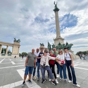 Eine WeRoad-Gruppe posiert gemeinsam auf einem großen Stadtplatz vor einem hohen Denkmal mit Statuen.