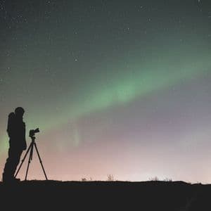Silhouette di un fotografo con la macchina fotografica su treppiede che osserva l'aurora boreale sotto un cielo stellato