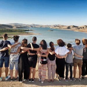 Eine WeRoad-Gruppe steht Arm in Arm und blickt über einen See, der von sanften Hügeln umgeben ist.