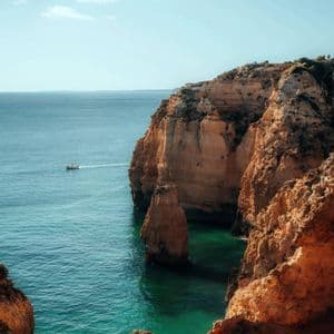 Una barca naviga su acqua turchese accanto a grandi scogliere arancioni sotto un cielo limpido.