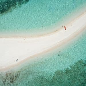 Una vista aerea di una lingua di sabbia bianca in acqua turchese, dove persone nuotano vicino a un kayak e una barca a bilanciere ormeggiata.