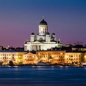 La Cattedrale illuminata di Helsinki e i palazzi sul lungomare della città, visti dall'acqua al crepuscolo.
