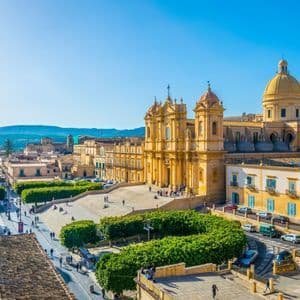 An elevated view of a historic city with a baroque cathedral and a grand staircase leading to a square with people walking.