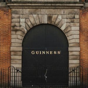 Un grande cancello ad arco nero con la scritta 'GUINNESS' in lettere dorate, inserito nella facciata di un edificio in pietra e mattoni.