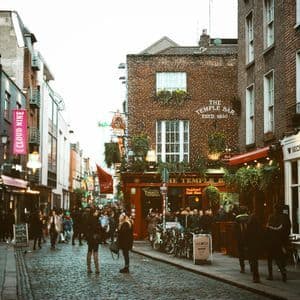 Una folla di persone su una strada di ciottoli di fronte a The Temple Bar, un pub storico in mattoni decorato con luci.