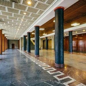 Una lunga sala con ampie colonne nere, un pavimento in marmo lucido con motivo geometrico e pareti rivestite in legno.