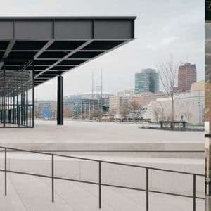 Un edificio moderno con una struttura in acciaio nero e pareti in vetro si erge su un'ampia piazza in cemento contro lo skyline della città.