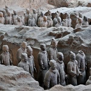 Estatuas de guerreros de terracota de tamaño natural se encuentran en formación en una fosa de excavación arqueológica, parcialmente cubiertas por tierra.