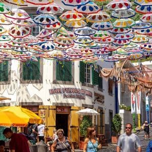Un baldacchino di ombrelli colorati a pois pende su una stretta via piena di persone e caffè all'aperto.