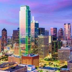 An expansive city skyline with illuminated skyscrapers under a colorful purple and pink sky at twilight.