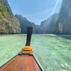 Una vista dalla prua di una barca tradizionale a coda lunga in legno che solca acque cristalline color turchese in una laguna circondata da alte scogliere verdi.