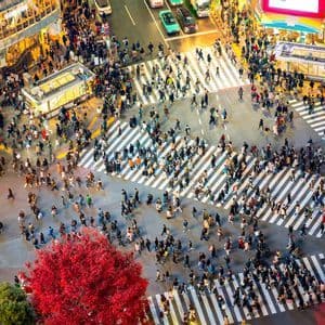 An aerial view of a large crowd of people crossing a busy, illuminated city intersection at night.