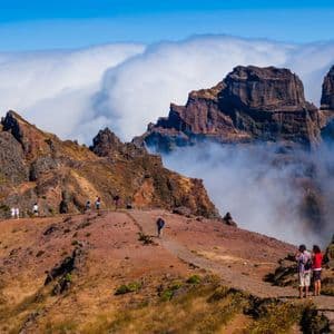 Eine WeRoad Gruppenreise wandert entlang eines gewundenen, felsigen Bergpfades mit zerklüfteten Gipfeln, die über einem Wolkenmeer aufragen.