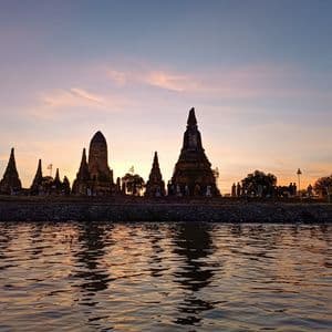 Silhouetten eines antiken Tempelkomplexes am Flussufer bei Sonnenuntergang, vom Wasser aus gesehen.