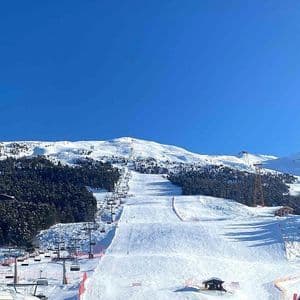 Un'ampia veduta di una montagna innevata con piste da sci e seggiovie sotto un cielo azzurro e limpido.