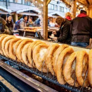 A long row of golden-brown fried pastries stands on a metal rack at a busy outdoor market stall.