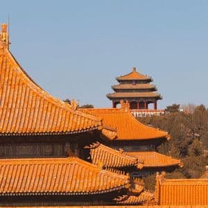 Tetti stratificati in tegole arancioni di un tradizionale complesso di templi cinesi, con una pagoda visibile su una collina alberata in lontananza, sotto un cielo sereno.