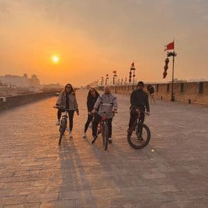 Quattro persone di un gruppo WeRoad in posa con le biciclette su un ampio muro di mattoni della città durante un tramonto nebbioso.