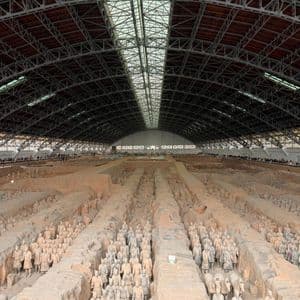 File di soldati dell'Esercito di Terracotta sono schierati in formazione nelle fosse scavate sotto il grande tetto ad arco di un museo.