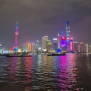 Uno skyline moderno di città di notte, con grattacieli illuminati da luci rosa e blu che si riflettono sull'acqua sottostante.