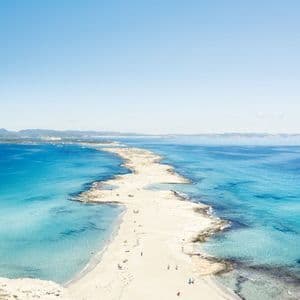 Eine Luftaufnahme einer schmalen Sandbank, die sich ins türkisfarbene Meer erstreckt, mit einem Segelboot, das vor der Küste unter klarem blauem Himmel ankert.
