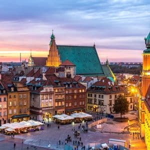 Vue surélevée d'une place historique européenne au crépuscule, avec des gens se promenant et dînant aux terrasses de café.