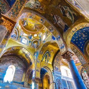 L'interno sontuoso di una chiesa con mosaici dorati e blu su volte e archi sostenuti da colonne di marmo.